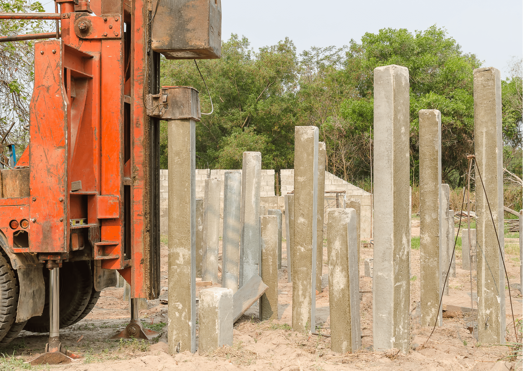 Piling Services | An orange truck pushing a construction pile down to the ground.