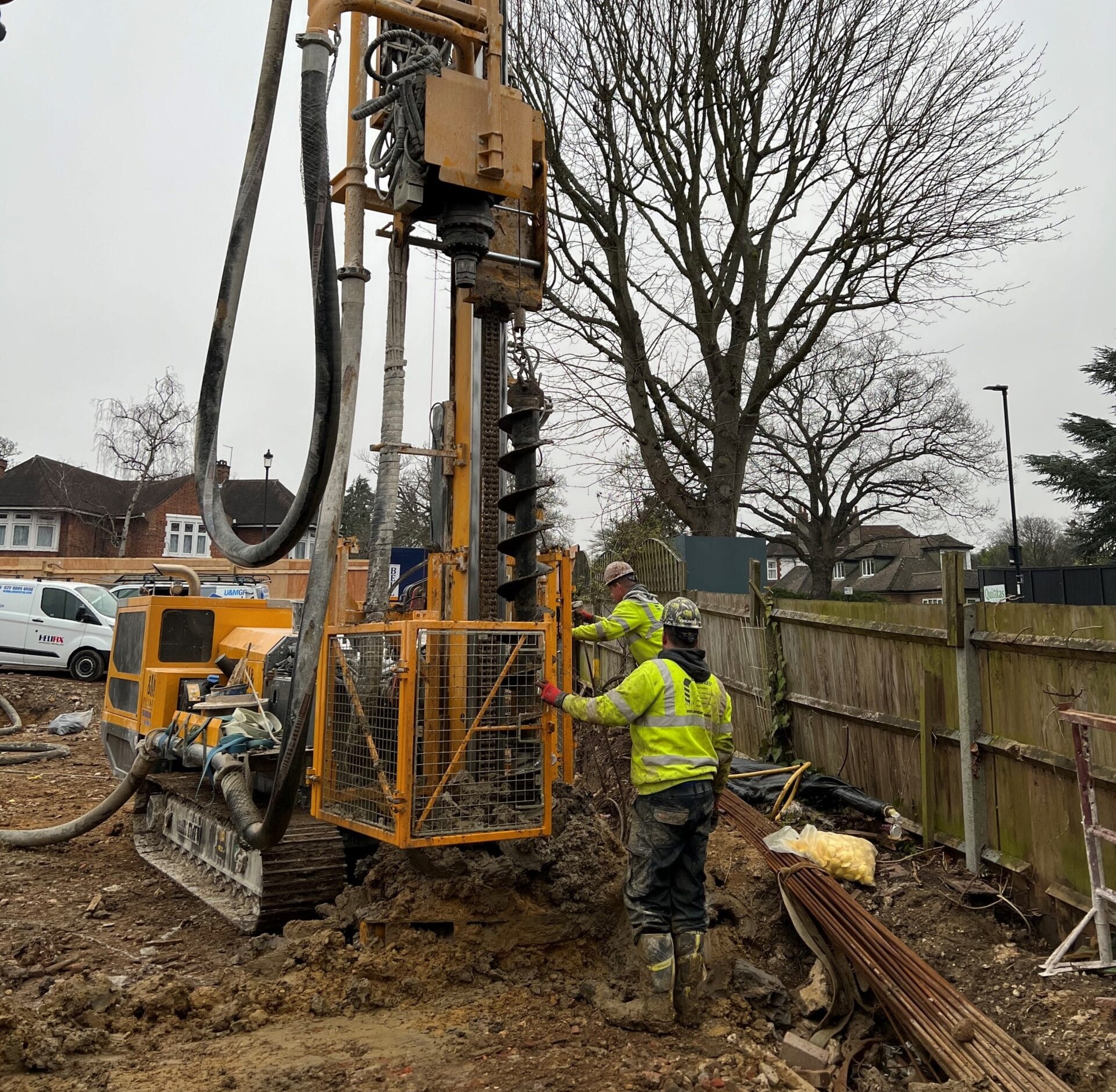 U&M Group offers piling services, here two workers are using piling machinery on a fenced yard.