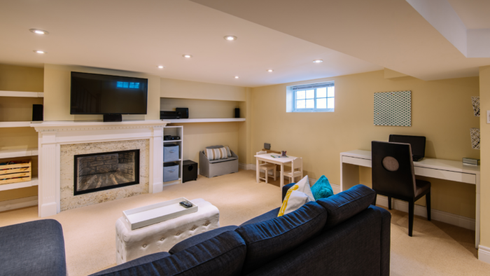 Retrofitting basement | Retrofitted basement with a blue sofa, work desk and a TV.